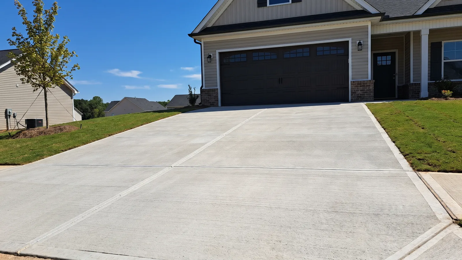 Finished broom-finish concrete driveway with saw-cut control joints leading to a two-car garage on a new subdivision home in Greer, South Carolina